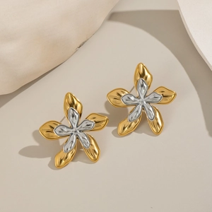 Macro shot of two-tone gold and silver flower stud earrings on a textured background