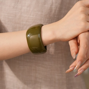 Detail view of a wide dark green resin bangle with smooth polished finish and artistic texture