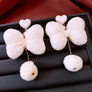 Elegant white bow earrings with pearl hearts and plush pompom drops on black tray