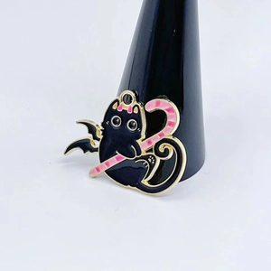 Cartoon black cat winged creature pin holding a pink candy cane on a display stand