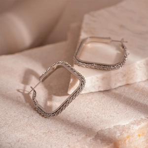 Minimalist square silver geometric hoop earrings with textured finish on marble display