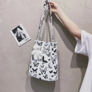 Close-up of white canvas tote bag with black butterfly prints and a plush bear charm