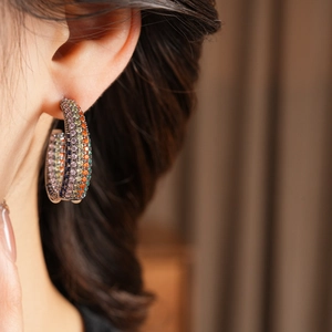 Macro shot of woman wearing large C-shaped earrings with colorful pave zircon stones