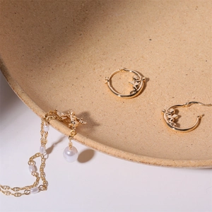 Golden cupid pendant pearl necklace and hoop earrings set on ceramic dishware