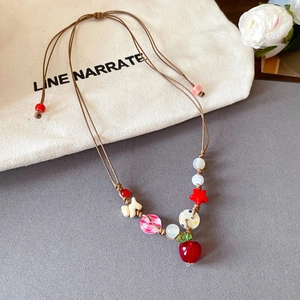 Collier tissé fait main avec perles colorées et pendentif pomme sur fond gris doux