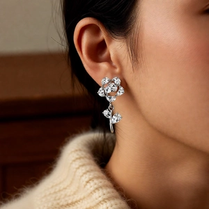 Close-up of elegant silver flower earrings with white zircons worn on ear in soft lighting