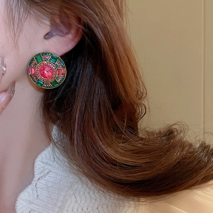 Close-up of a vintage gold earring with a pink center stone and emerald green halo