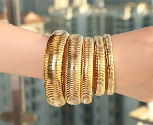 Close-up of stacked gold tubogas snake bone elastic bracelets in various widths on wrist