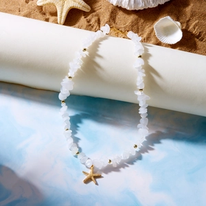 Detail of bohemian gravel beaded necklace with gold starfish pendant on beach background