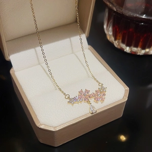 Detail of a gold floral necklace with pink crystals and a teardrop pendant in a gift box