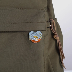 Detailed close-up of a heart-shaped dog enamel pin on a green canvas backpack strap