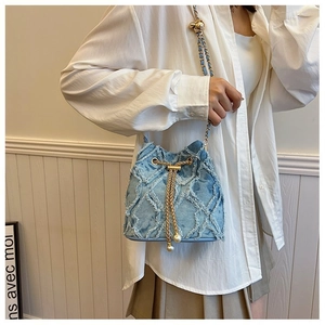 Detail of blue denim bucket bag with gold chain strap and pearl drawstring accents