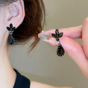 Detail shot of elegant black teardrop earrings with leaf motifs on a warm grey background