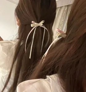 Close-up of a cream satin bow hair clip with long ribbons worn on the back of the head