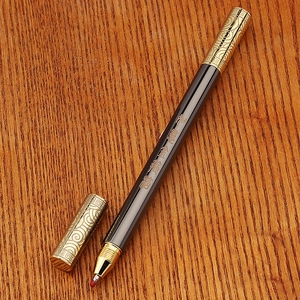 Detail of vintage brass bamboo pen with gold floral engraving on a wooden desk