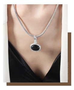 Silver snake chain necklace with black oval pendant worn by a model in a white blazer