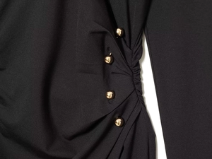 Detail eines schwarzen V-Kleides mit plissiertem Stoff und goldenen Kugelknöpfen Verzierungen