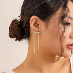 Detailed view of silver bow earrings with sparkling tassels worn by a model