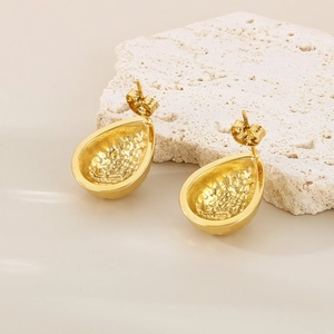 Macro detail of golden teardrop earrings with textured inner surface on a white stone