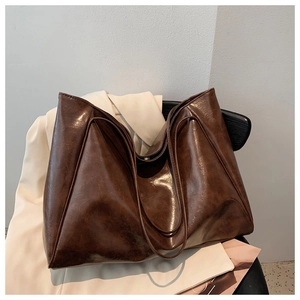 Detail of a large dark brown faux leather tote bag on a chair with a blazer background