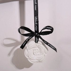 White camellia plaster aroma stone diffuser with black ribbon hanging on light background