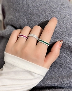 Primo piano di anelli impilati in argento S925 con zirconi rossi, bianchi e verdi sul dito