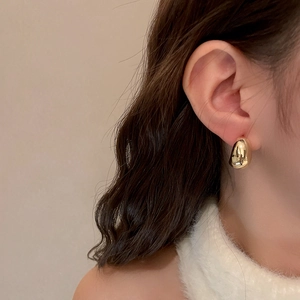 Minimalist golden C-shaped droplet earrings with a polished metallic finish on model