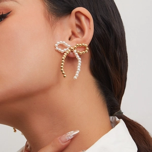 Close-up of elegant gold bow earrings with imitation pearls worn by a model