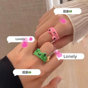 Close-up of cute green and pink resin frog open rings worn on fingers in playful style