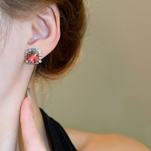 Close-up of elegant silver stud earrings with a red gemstone and crystal halo on a model