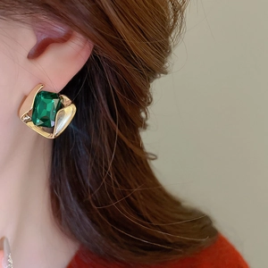 Close-up of vintage golden geometric earrings with emerald green crystals on model