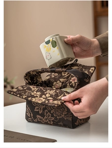 Detail of a ceramic rabbit tea jar being placed into a gold floral fabric carry bag