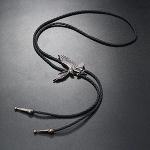 Detailed view of an eagle pendant bolo tie with black braided cord on a textured surface