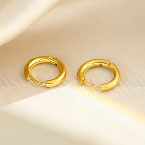 Detailed close-up of golden hoop earrings on elegant beige silk fabric background