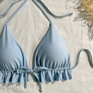 Detail of light blue halter bikini top with ruffled hem and drawstring ties on linen