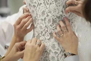 Gros plan d'artisans ajustant la dentelle florale complexe d'une robe de mariée blanche de luxe