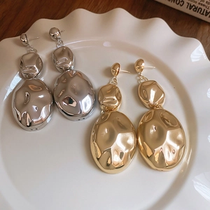 Close-up of gold and silver irregular oval metal earrings on a white wavy plate