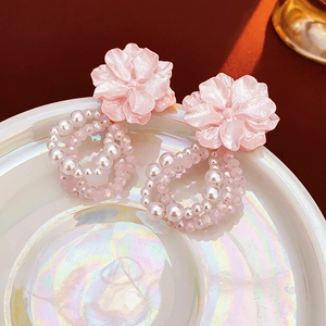 Close-up of pink flower earrings with woven pearl circles on a reflective plate
