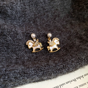 Macro shot of gold-plated rocking horse earrings with pearls and shimmering zircons
