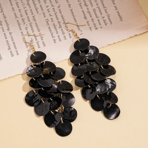Close-up of black geometric shell tassel earrings with layered round discs and gold hooks
