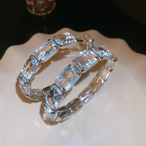 Macro shot of large silver hoop earrings with rectangular crystals on a white ceramic tray