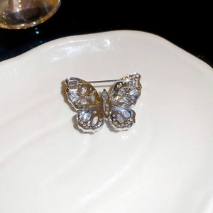Macro detail of silver butterfly brooch with teardrop zircons on white ceramic plate