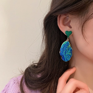 Close-up of model wearing irregular blue heart earrings with textured metallic finish