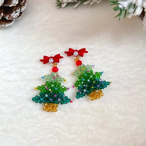 Christmas tree earrings with green beads and red bow on white plush background