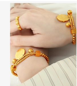 Detail view of gold beaded bracelets with engraved charms and 18k gold cube accents
