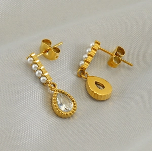 Detailed view of gold drop earrings with pearls and faceted zircon on grey silk