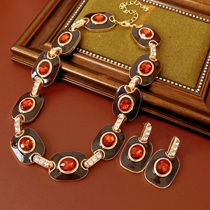 Vintage gold jewelry set with black enamel and orange gemstones displayed on wood