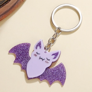 Purple glittery acrylic bat keychain with metal ring accessory on a beige background