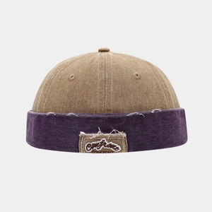 Detailed macro view of stitched 'Confront' patch on two-tone khaki and purple docker cap