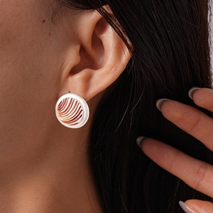 Close-up of retro geometric round stud earrings with orange radial texture on white enamel